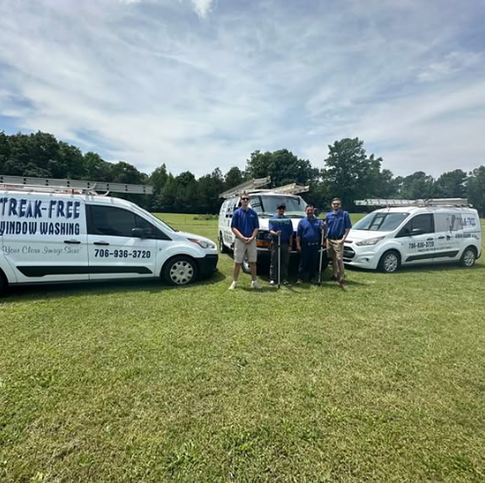 Three people in navy shirts standing on a lawn between two white Streak-Free vans